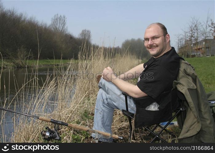 Fisherman sitting by the side of the water with a happy smile on his face