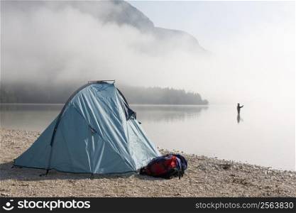 Fisherman standing in a mountain lake with his tent in the foreground