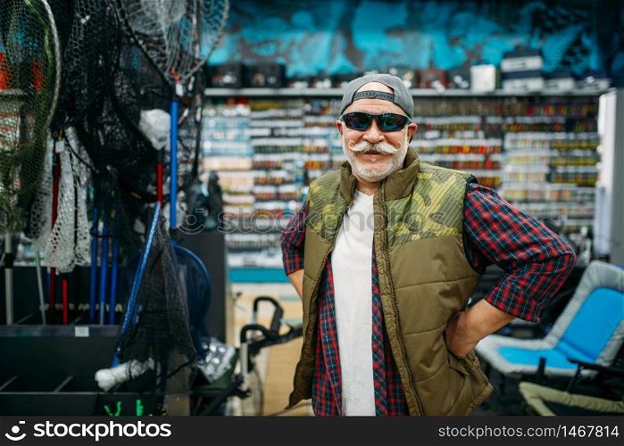 Fisherman tries on sunglasses in fishing shop. Equipment and tools for fish catching and hunting, accessory choice on showcase in store. Fisherman tries on sunglasses in fishing shop
