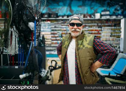 Fisherman tries on sunglasses in fishing shop. Equipment and tools for fish catching and hunting, accessory choice on showcase in store. Fisherman tries on sunglasses in fishing shop
