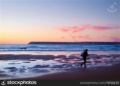 Fisherman walking on the ocean beach at sunset. Portugal