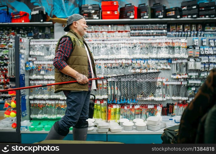 Fisherman with net and toolbox in fishing shop, hooks and baubles on background. Equipment and tools for fish catching and hunting, accessory choice on showcase in store, bait assortment. Fisherman with net and toolbox in fishing shop