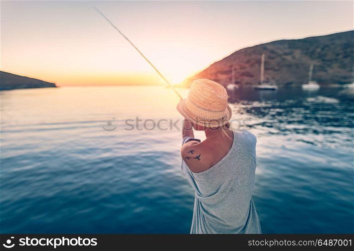 Fisherman woman standing with fishing rod on the sea coast and trying to catch a fish, traditional summer hobby of active people, happy weekend on the beach. Fisherman woman