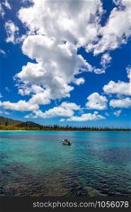 Fishing boat anchored by a tropical island with blue sky and white clouds in the background.