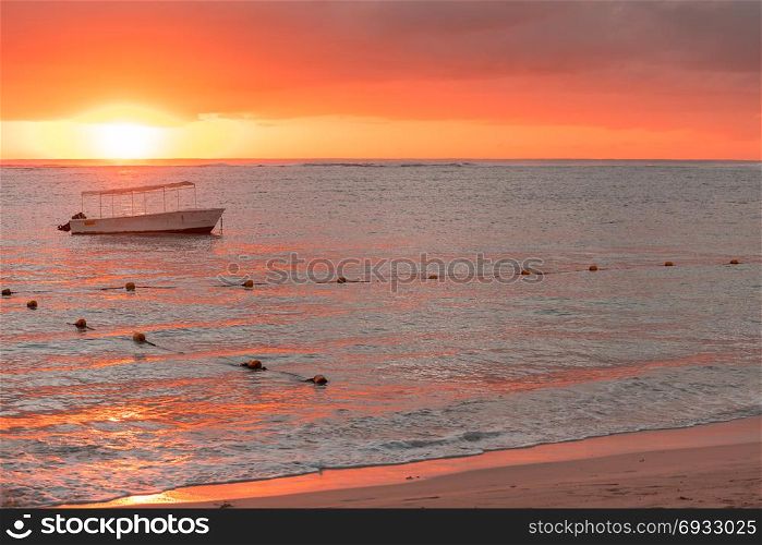 Fishing boat anchored near the shore of the beach at orange sunset,mauritius beach Flic and Flac.