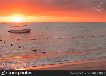 Fishing boat anchored near the shore of the beach at orange sunset,mauritius beach Flic and Flac.