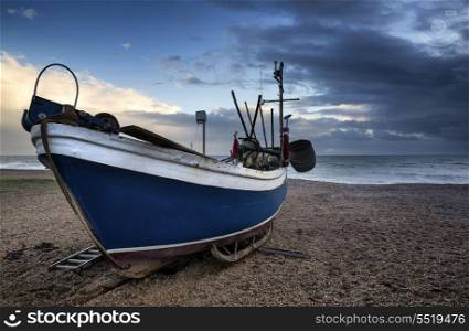 Fishing boat on shingle beach landscape with stormy sky