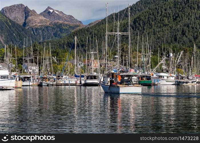 Fishing boat sailing in marina and is about to dock. Marina full of other fishing boats. Gorgeous mountains and forest in the background. Sitka, Alaska, USA