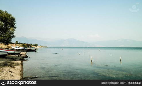 Fishing boats on coast of Lake Prespa and Mountains of Galicica National Park. Prespa lake is situated between Macedonia, Greece and Albania, known of it&rsquo;s wild nature and pelican reserve.. Fishing boats on coast of Lake Prespa and Mountains of Galicica National Park.