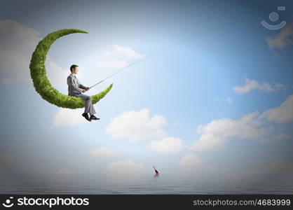 Fishing concept. Businessman sitting on green moon and fishing with rod