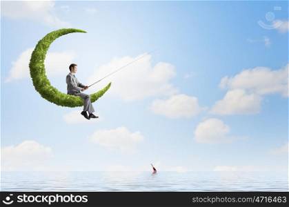 Fishing concept. Businessman sitting on green moon and fishing with rod