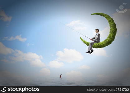 Fishing concept. Businessman sitting on green moon and fishing with rod