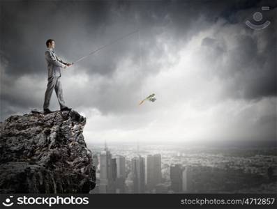 Fishing concept. Businessman sitting on rock and fishing with rod