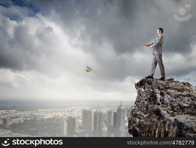 Fishing concept. Businessman sitting on rock and fishing with rod