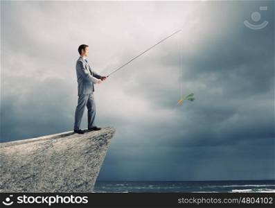 Fishing concept. Businessman sitting on rock and fishing with rod