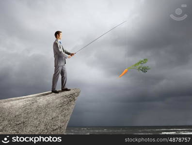 Fishing concept. Businessman sitting on rock and fishing with rod