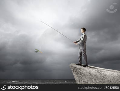 Fishing concept. Businessman sitting on rock and fishing with rod