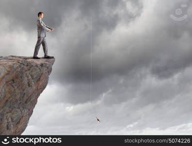 Fishing concept. Businessman sitting on rock and fishing with rod