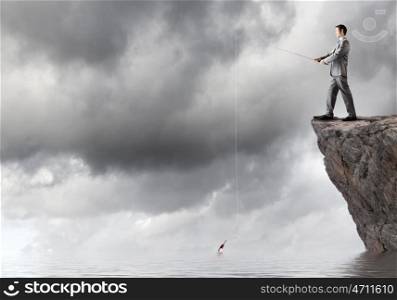 Fishing concept. Businessman standing on rock and fishing with rod