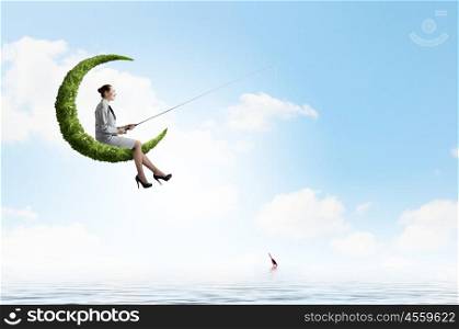 Fishing concept. Businesswoman fishing with rod on green moon