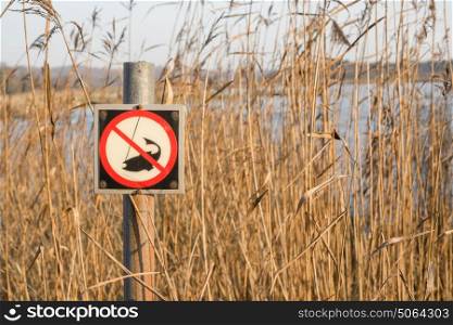 Fishing forbidden sign by a lake in the autumn with tall reeds in the background and a post with a fishing prohibition symbol