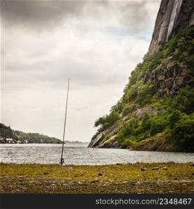 Fishing rod left alone on shore near lake and mountains. Cloudy scandinavian weather.. Fishing rod left alone on lake shore