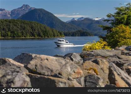 Fishing speedboat sailing fast in harbor. Beautiful yellow trees and rocks in soft focus in the foreground. Mountains, and forest in the background. Sitka, Alaska, USA