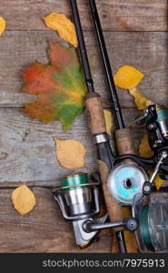 fishing tackles reel, line and lure on wooden board with leafs of autumn