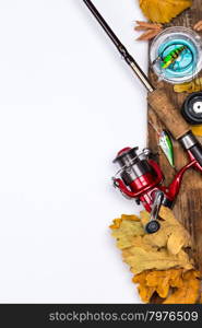 fishing tackles reel, line and lure on wooden board with leafs of autumn