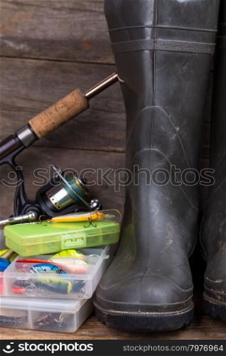 fishing tackles rod, reel, wobblers in boxes with rubber boots on timber board background. for design advertising or publication
