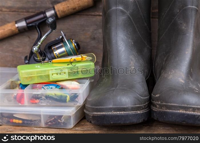 fishing tackles rod, reel, wobblers in boxes with rubber boots on timber board background. for design advertising or publication