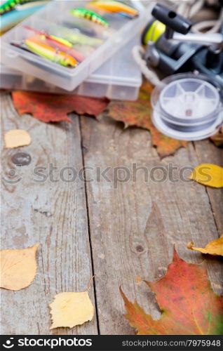 fishing tackles wobblers and lures in box on wooden board with leafs of autumn