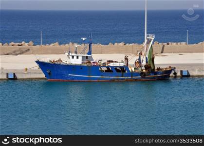Fishing trawler in port. Rusty dragger ship tied to shore.
