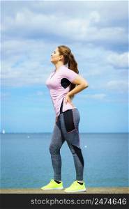 Fit attractive young woman wearing fashionable outfit working out being active outside next to sea. Woman exercising next to sea