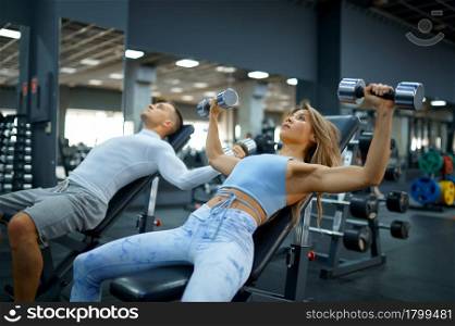 Fit couple doing exercise with dumbbells, fitness training in gym. Athletic man and woman on workout in sport club, active healthy lifestyle, physical wellness. Fit couple doing exercise with dumbbells in gym