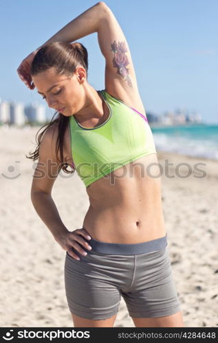 Fit hispanic woman stretches on the beach after a run