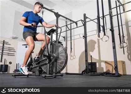 Fit man doing cardio training on stationary air bike machine with fan at the gym. High quality photo. Fit man doing cardio training on stationary air bike machine with fan at the gym.
