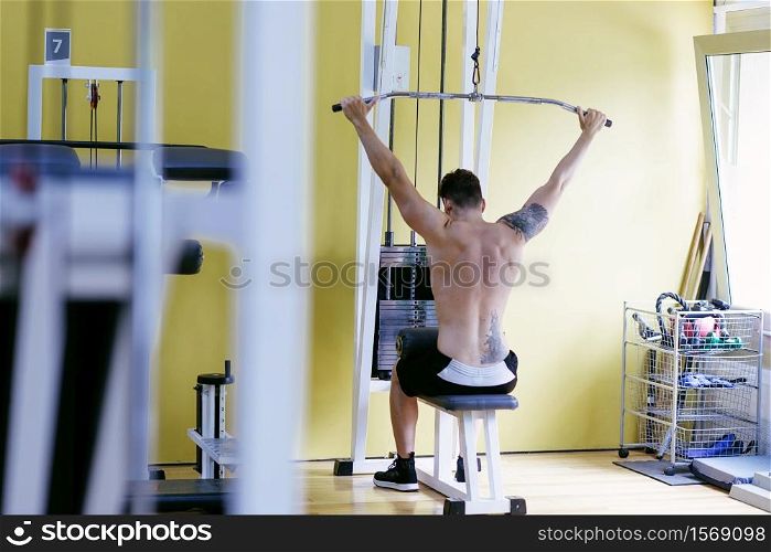 Fit man on lat pull down machine at the health club. Work out on Pull down Weight Machine. DanielFernandez.jpg,tatoo.jpg,SquashCardedeu.jpg