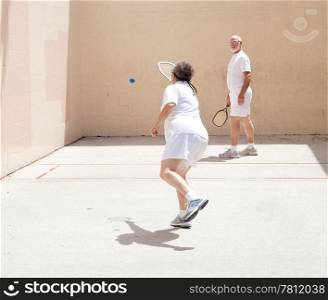Fit senior couple playing racquetball together on a public court.