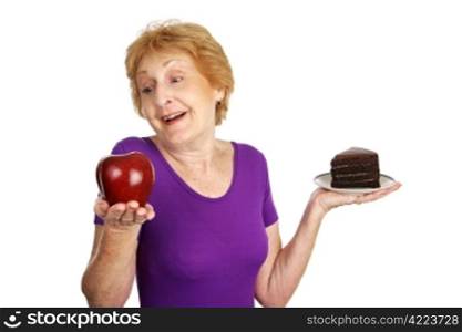 Fit senior lady choosing a healthy apple for dessert instead of fattening chocolate cake. Isolated on white.