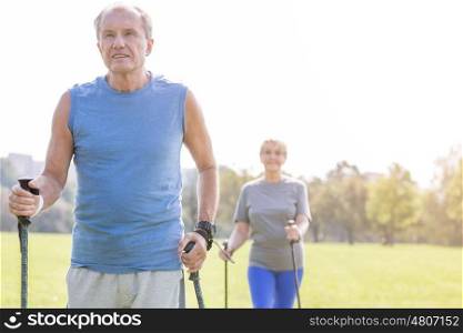 Fit senior male using trekking poles with woman in park