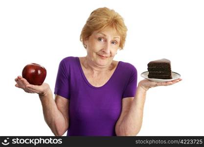 Fit senior woman choosing between chocolate layer cake and an apple for dessert. Isolated on white.