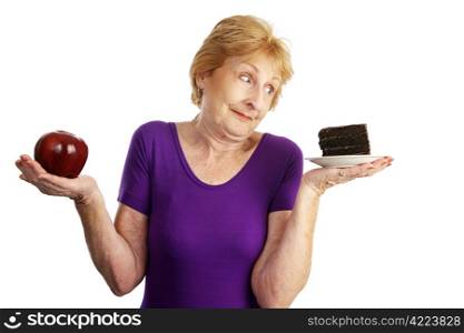 Fit senior woman making food choices. She is unable to resist the chocolate cake. Isolated on white.