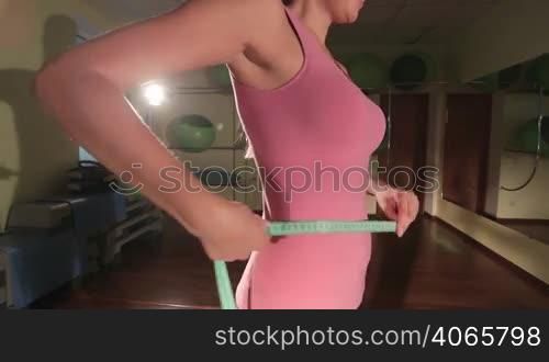 Fit slim woman measuring waist with measure tape after fitness workout in gym