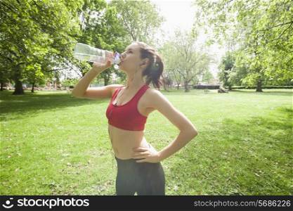 Fit woman drinking water while listening to music in park
