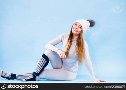 Fit woman in full length wearing winter cap, gray sports thermal underwear, warm socks studio shot on blue. Long sleeves top and leggings.. woman in thermal underwear top ang leggings