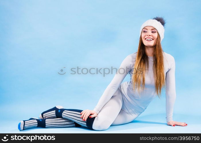 Fit woman in full length wearing winter cap, gray sports thermal underwear, warm socks studio shot on blue. Long sleeves top and leggings.