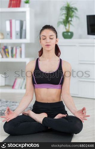 fit woman meditating in lotus pose in the living room