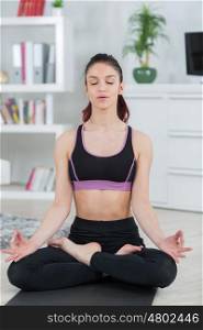 fit woman meditating in lotus pose in the living room