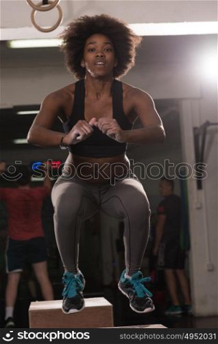 Fit young african american woman box jumping at a crossfit style gym. Female athlete is performing box jumps at gym.